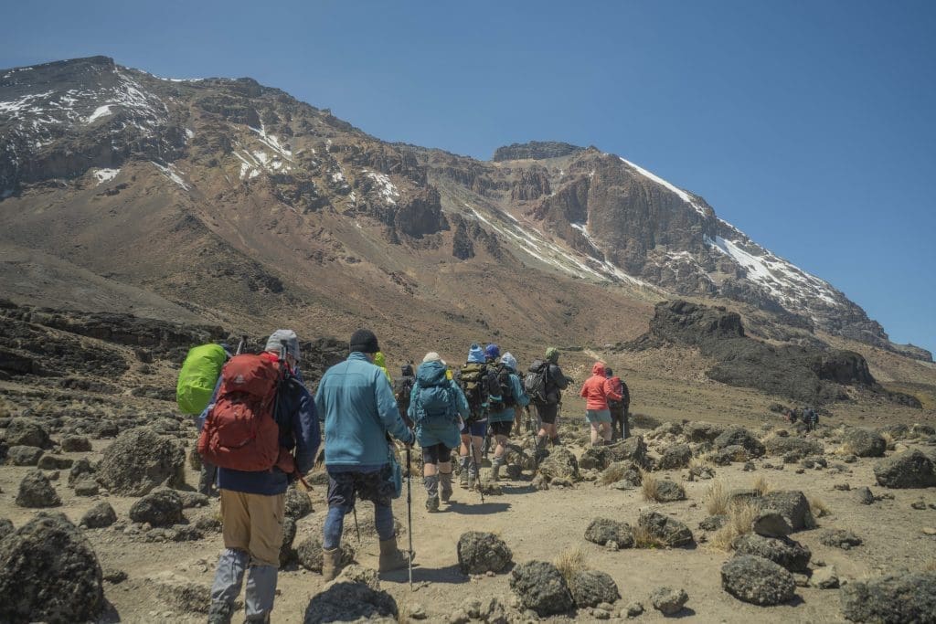 Climbers trekking towards Mount Kilimanjaro’s summit across rocky terrain with the mountain peak in the background.