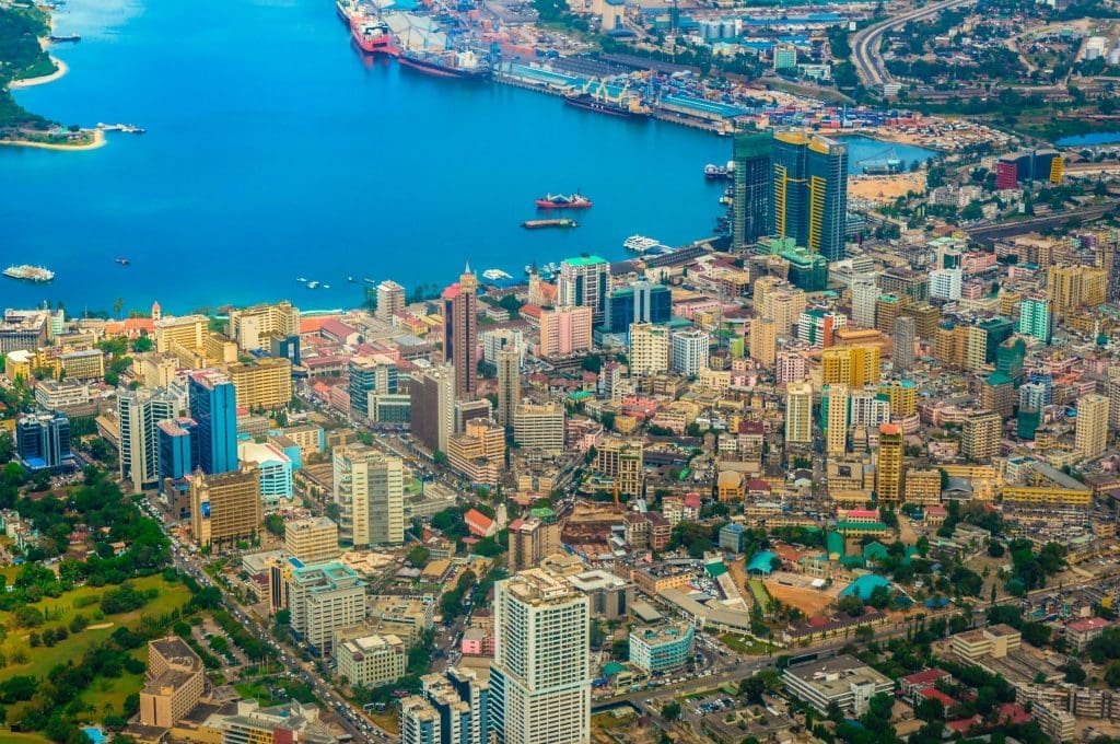 Aerial view of Dar es Salaam city showing the coastal skyline, high-rise buildings, busy port, and the Indian Ocean waterfront.